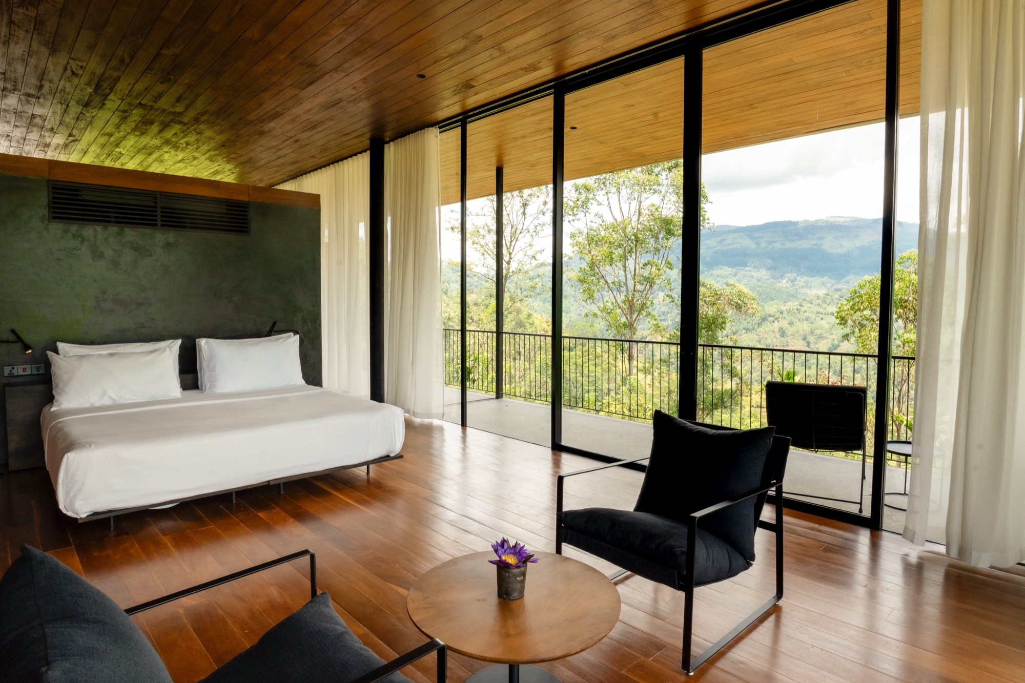 Villa bedroom with a low bed, timber floor and floor-to-ceiling glass onto the mountains