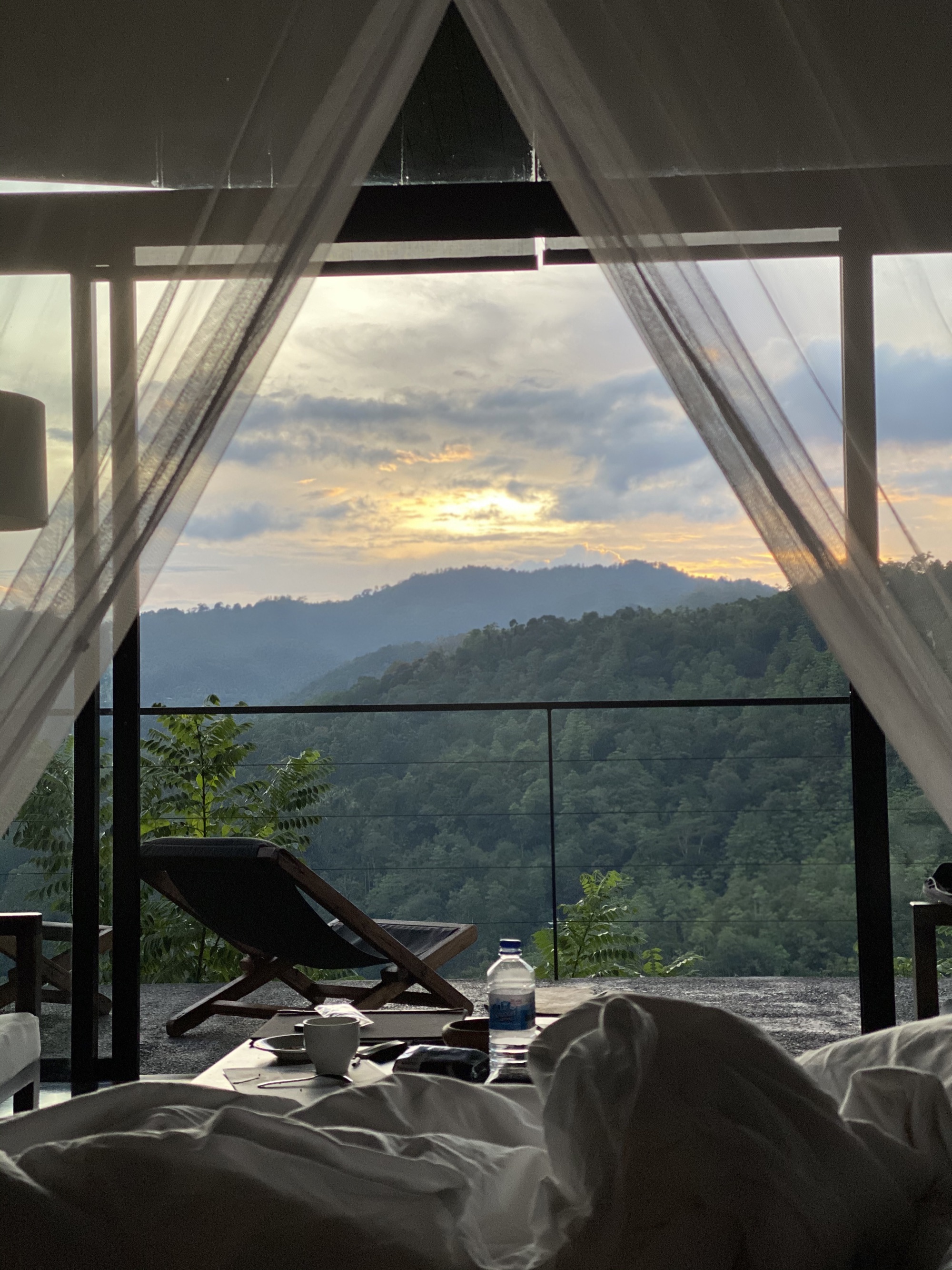 View from a chalet bed through the mosquito net to loungers and mountains at sunrise