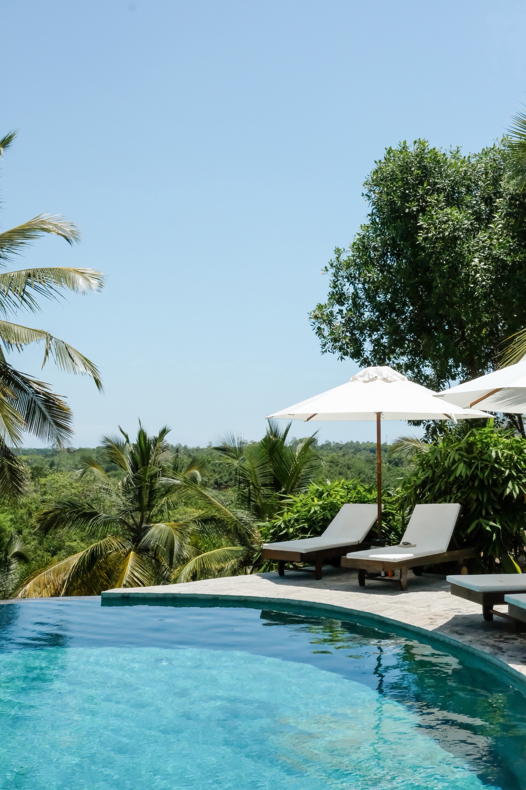 Poolside loungers and umbrella beside the infinity pool under a clear sky