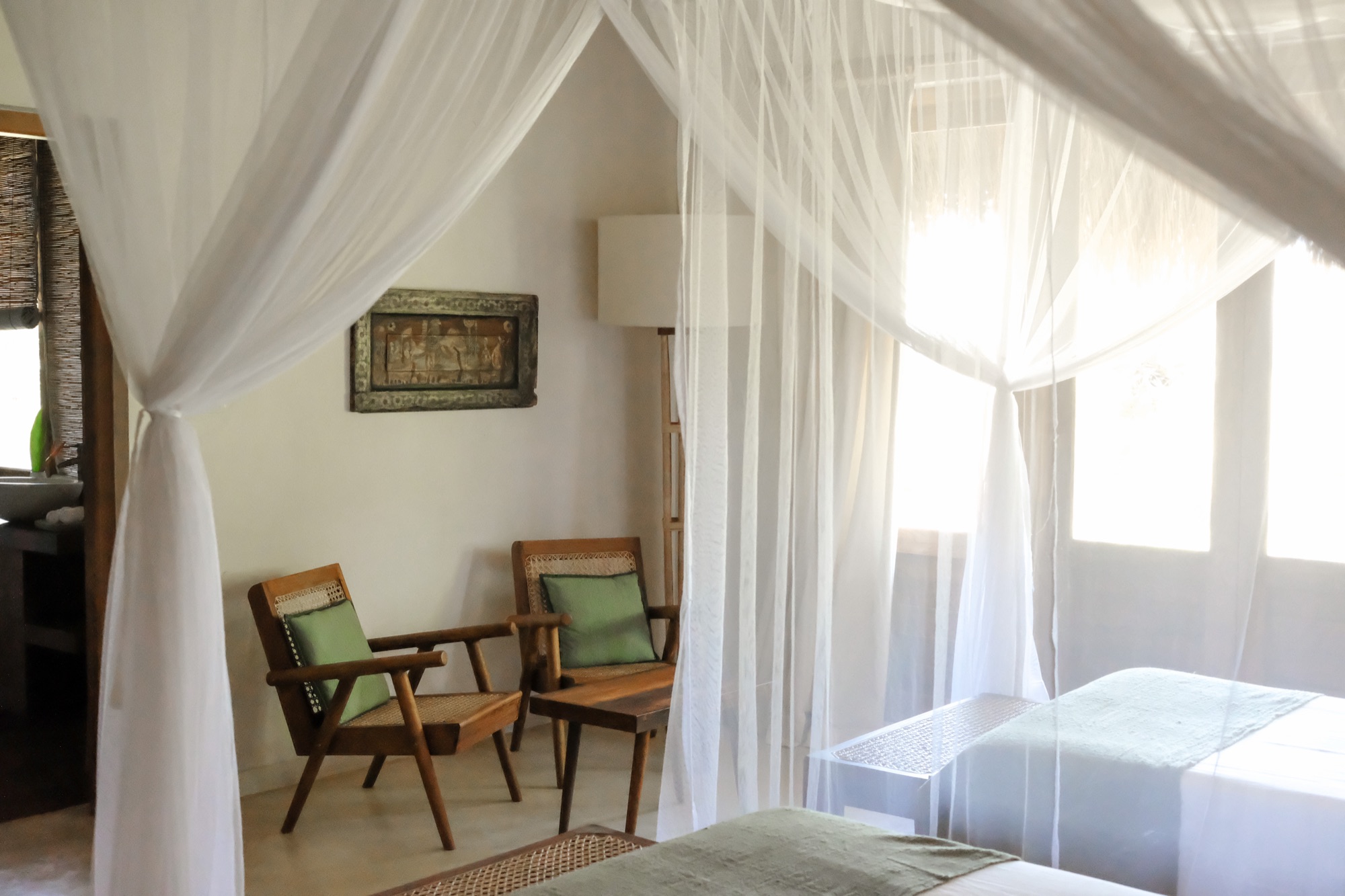 Bedroom with white mosquito-net canopies over twin beds and cane armchairs
