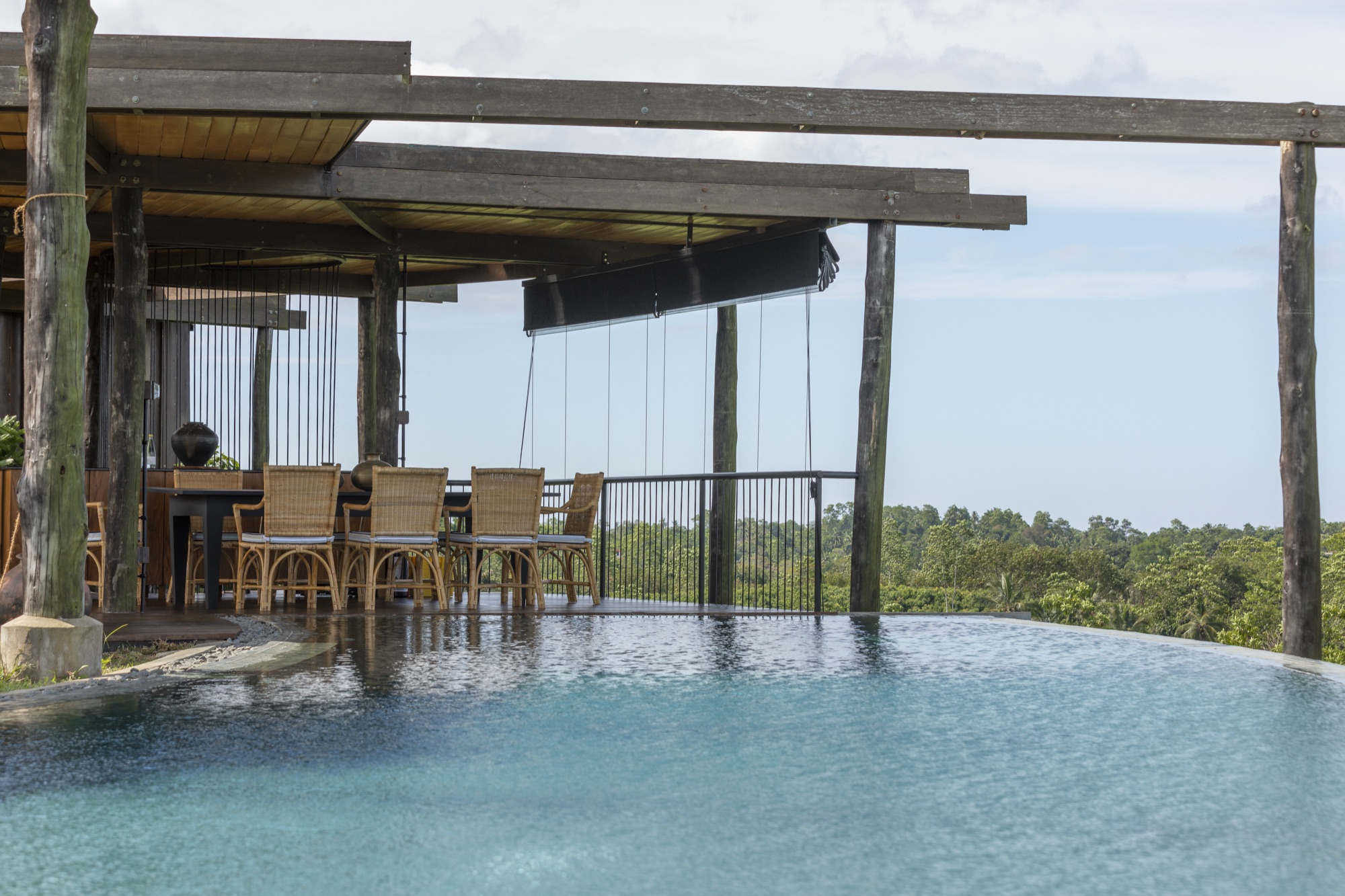 Infinity pool beside a timber pergola dining terrace overlooking the jungle