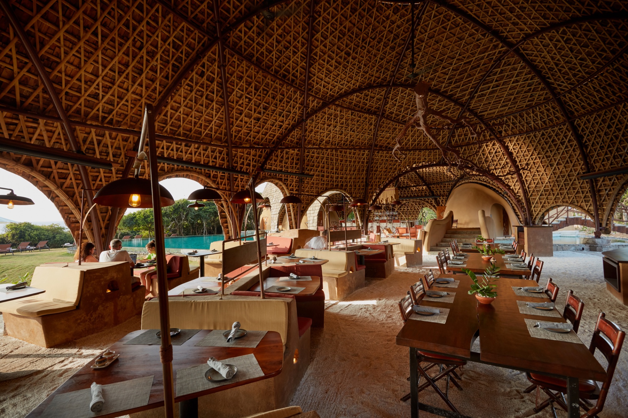 Le restaurant à ciel ouvert sous une voûte de bambou tressé, avec la piscine aperçue à travers les arches