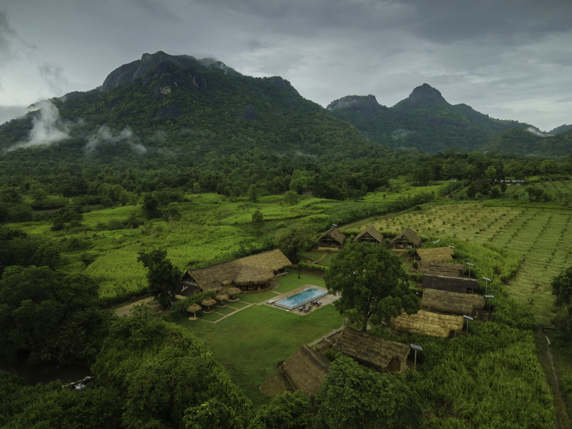 Wide aerial view of the property in a green valley with mist-wrapped mountains behind