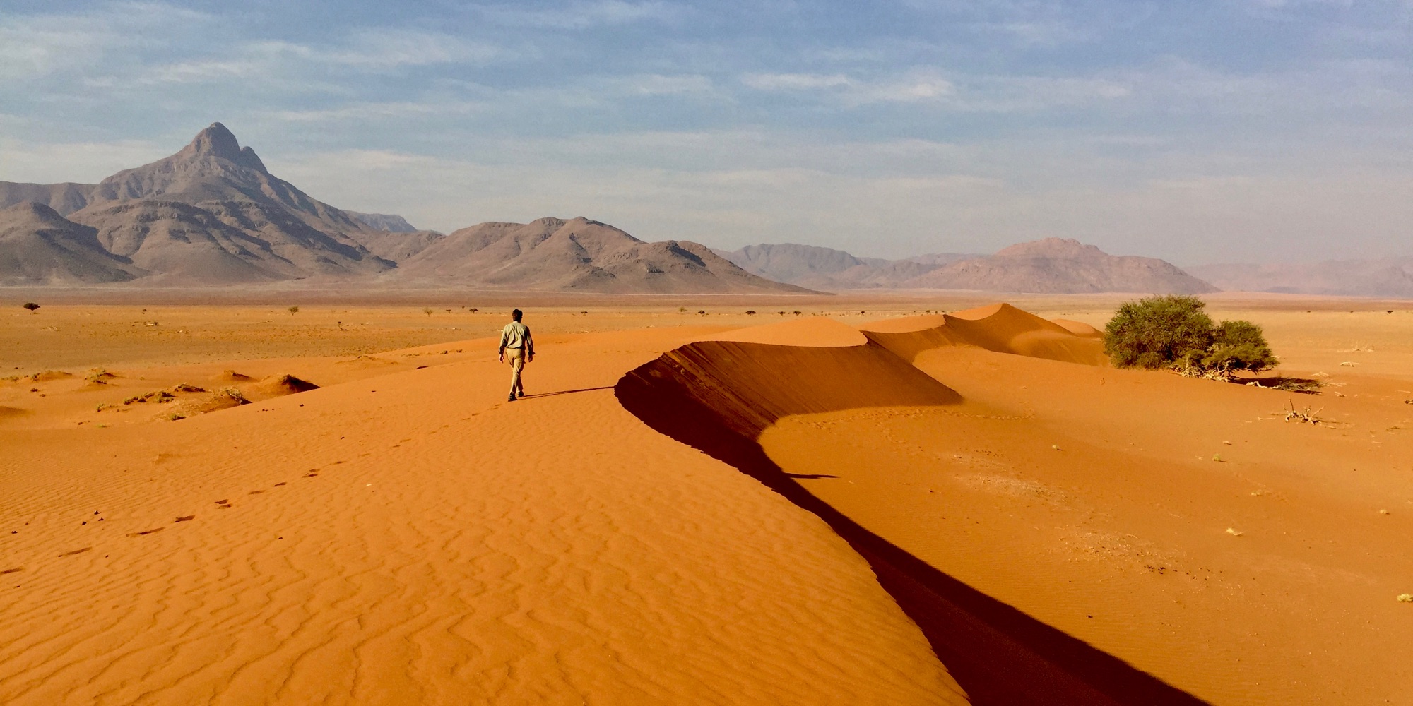 A walker on a red dune ridge, mountains behind