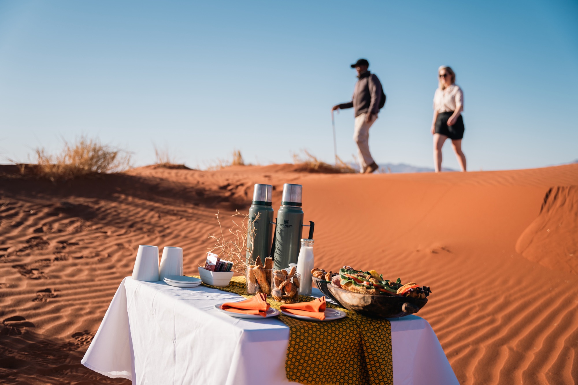 Coffee table set on a red dune as two guests walk the crest