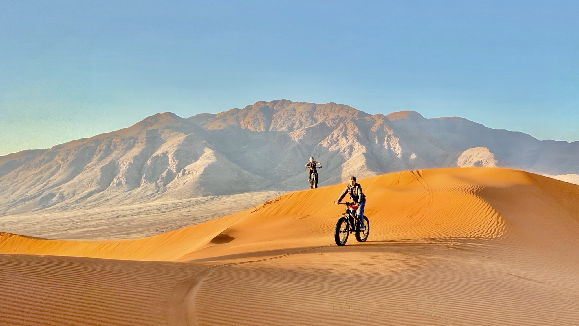 Fat e-bikes riding over the dunes below a mountain