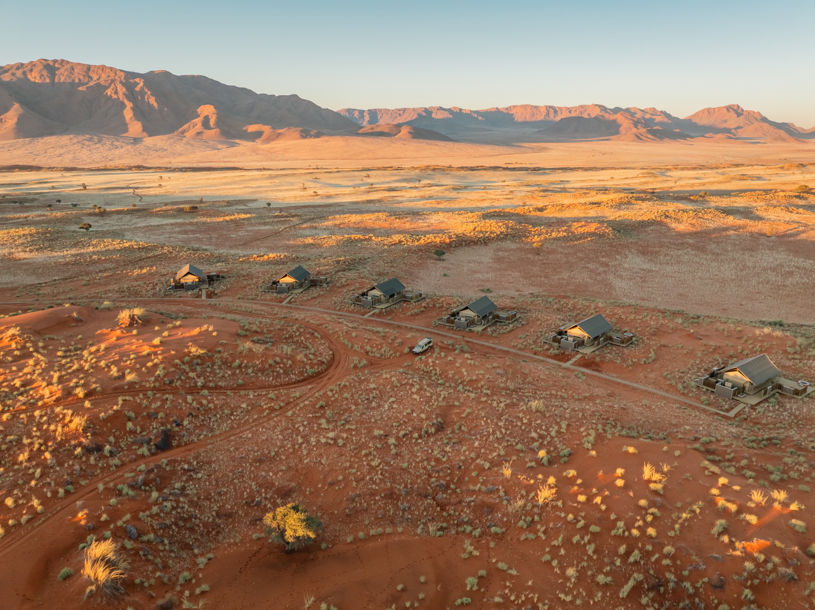 Tented rooms in a line on the red sand, mountains on the horizon — Wolwedans Dune Camp, NamibRand Nature Reserve, Namibia
