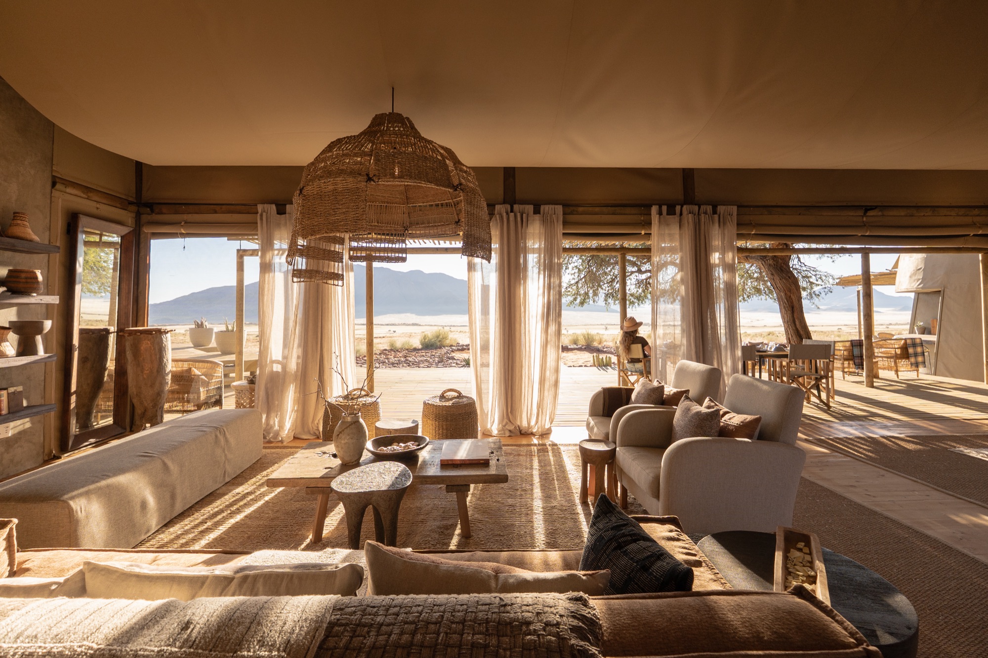 Lounge with linen curtains, wicker lamps and armchairs opening onto the desert