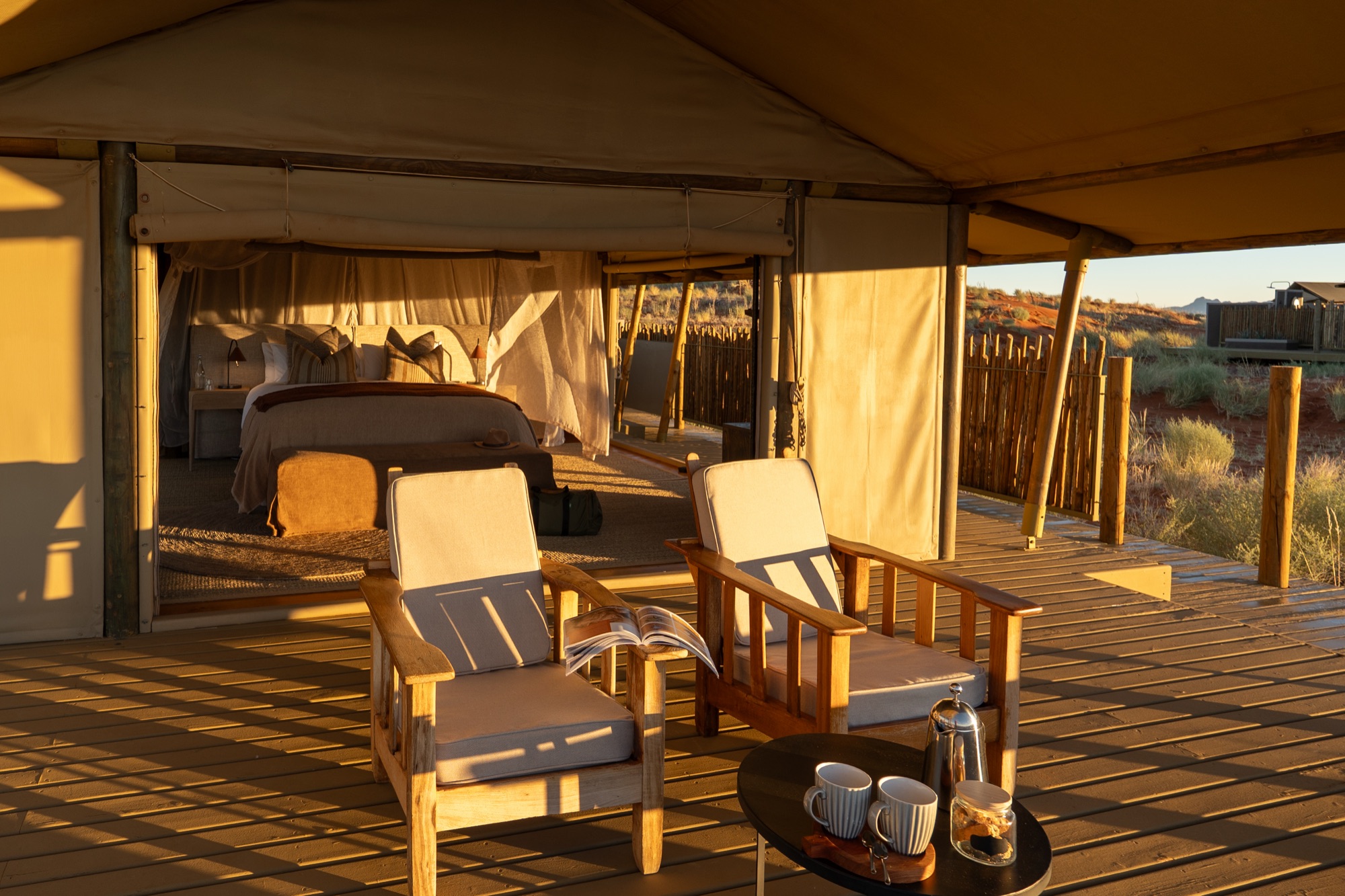Two armchairs and coffee on a tented room deck in morning light