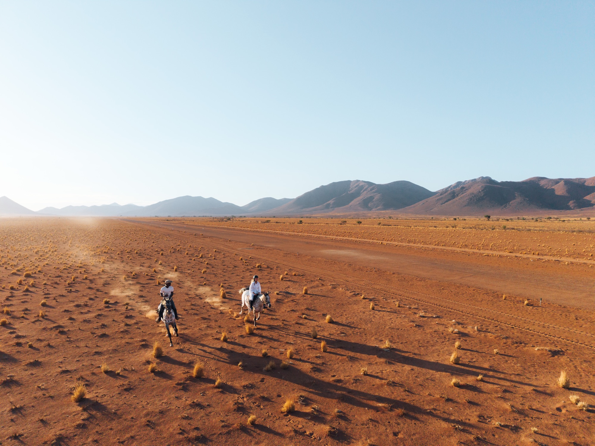 Two riders crossing the red sand, seen from above