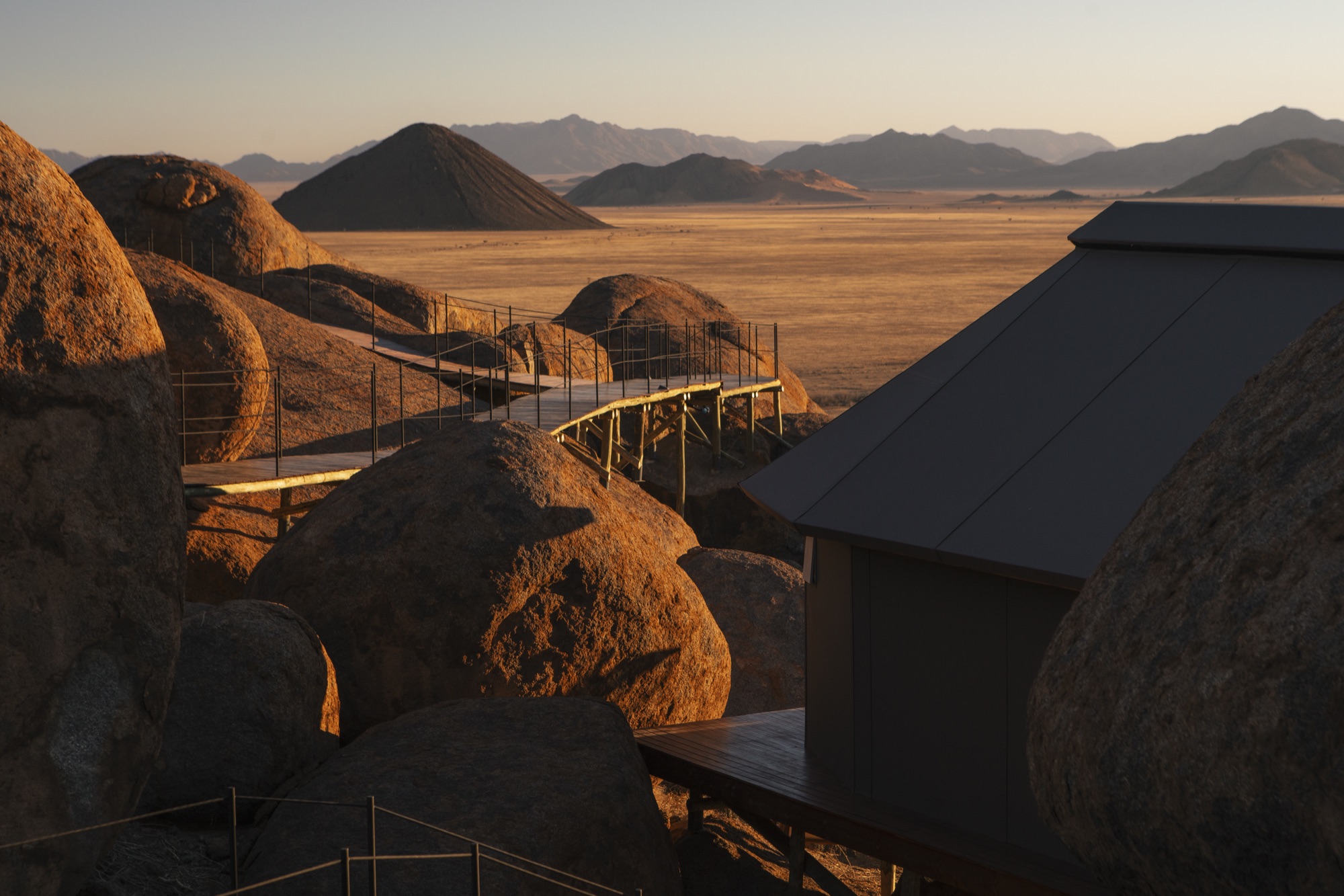 A tent and its walkway among the boulders, a cone-shaped hill on the horizon