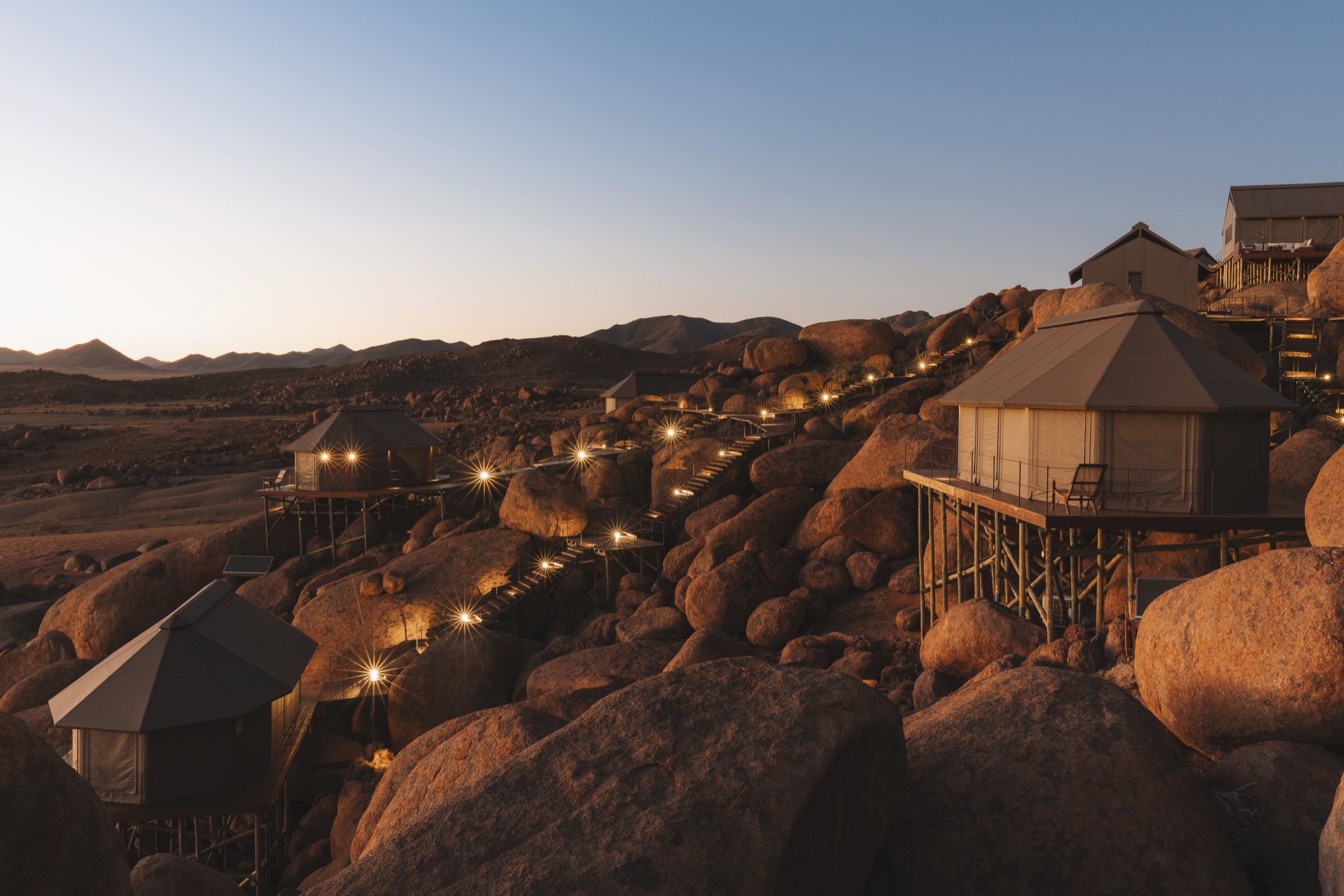 Tents on stilts lit up among the boulders at dusk