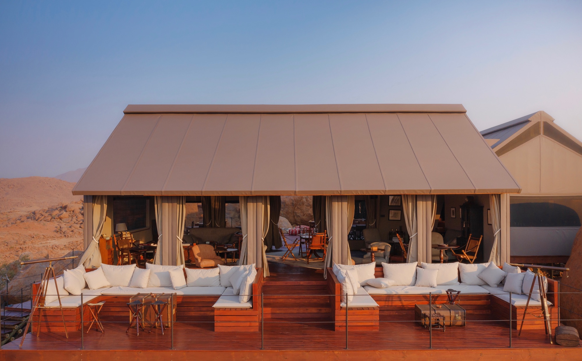 Open-sided lounge tent with white sofas on a wooden deck